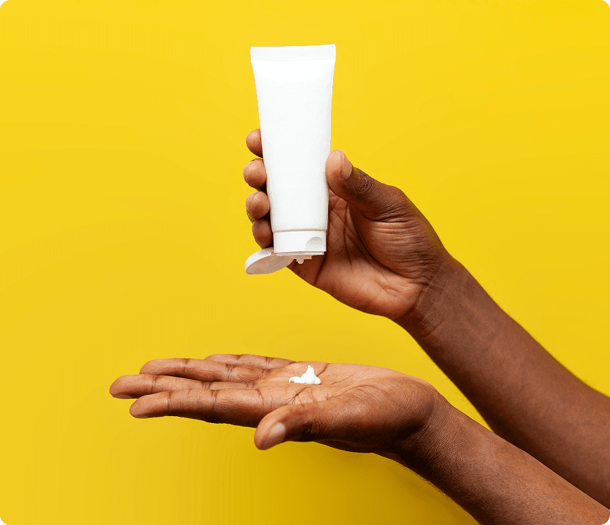 Hand holding lotion tube on yellow background.